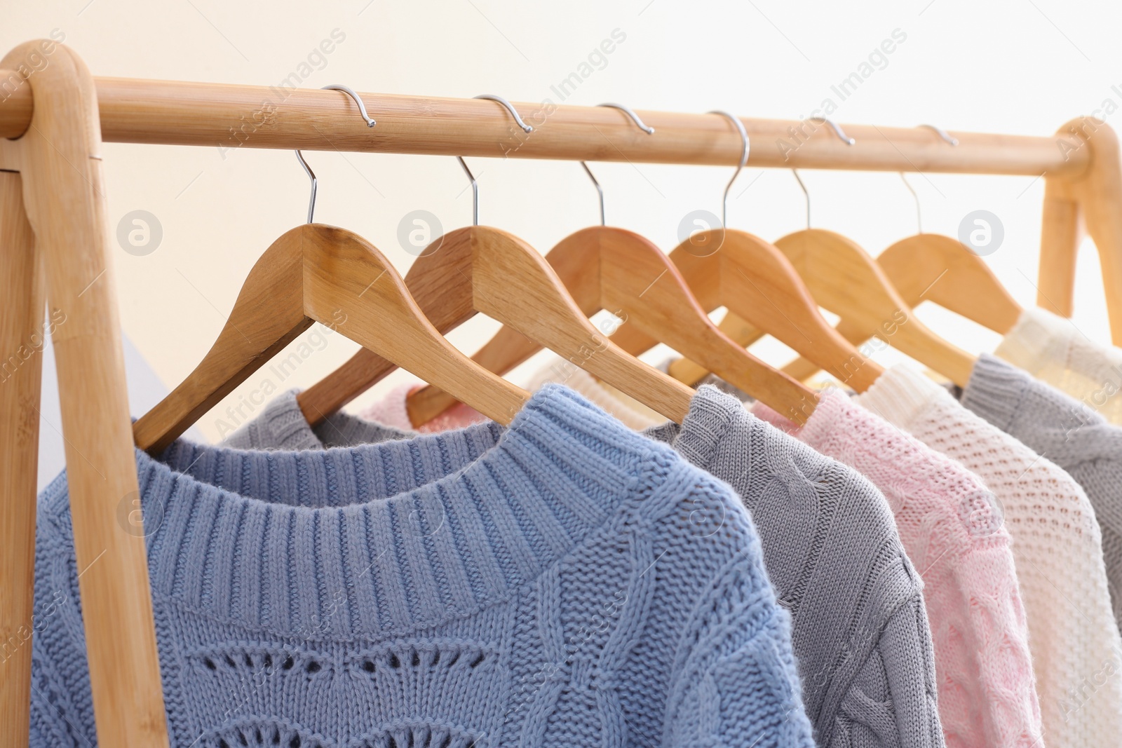 Photo of Collection of warm sweaters hanging on rack near color wall, closeup