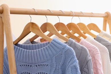 Photo of Collection of warm sweaters hanging on rack near color wall, closeup