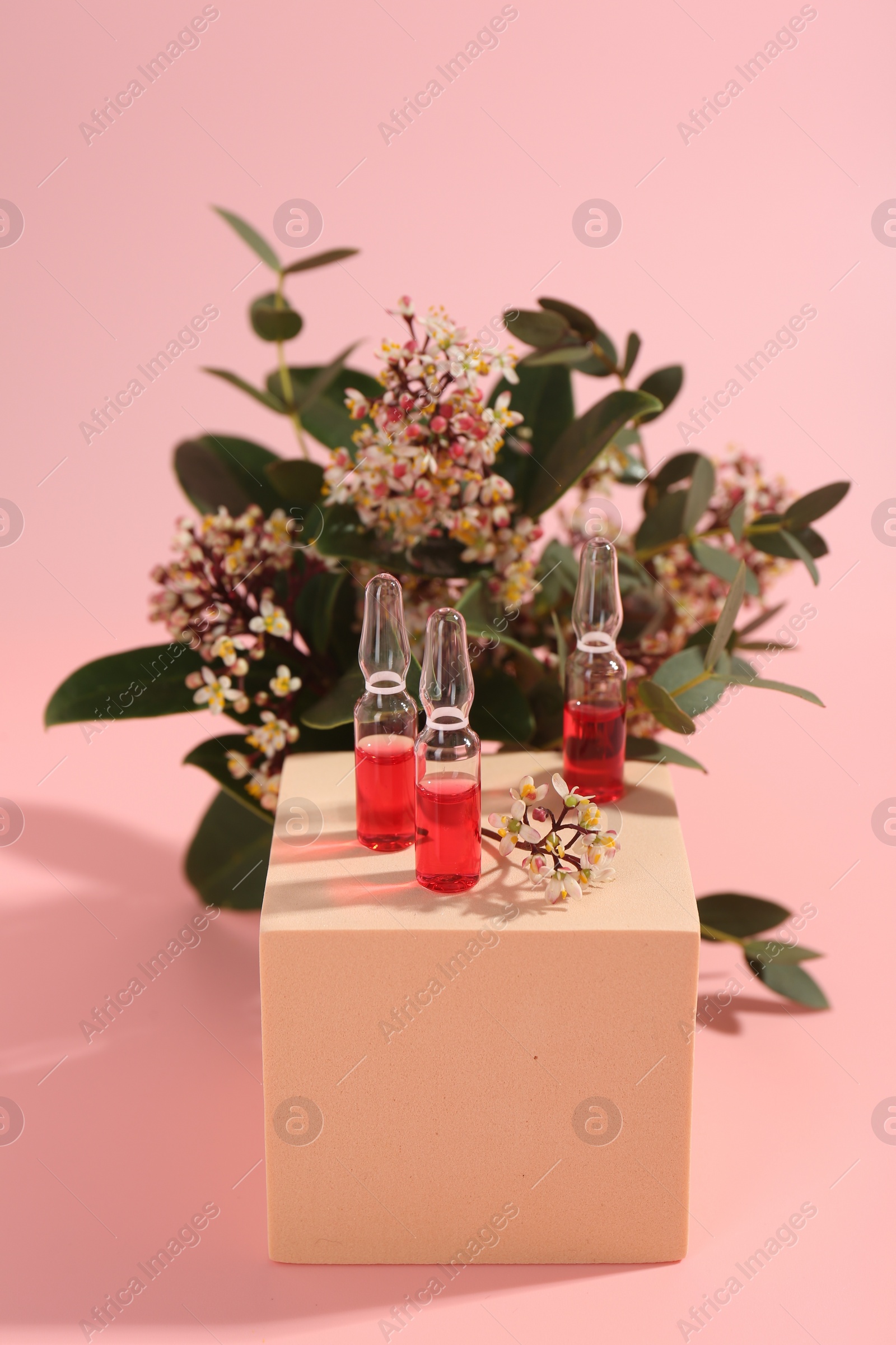 Photo of Stylish presentation of skincare ampoules and flowers on pink background