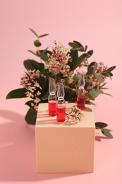 Photo of Stylish presentation of skincare ampoules and flowers on pink background