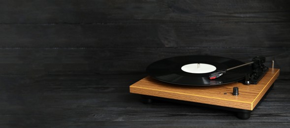 Photo of Turntable with vinyl record on black wooden background. Space for text