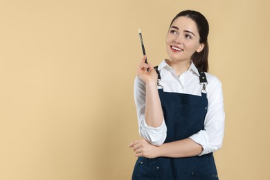 Woman with paintbrush on beige background, space for text. Young artist