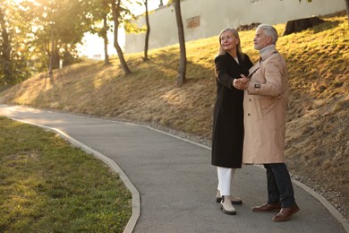 Photo of Affectionate senior couple dancing together outdoors, space for text