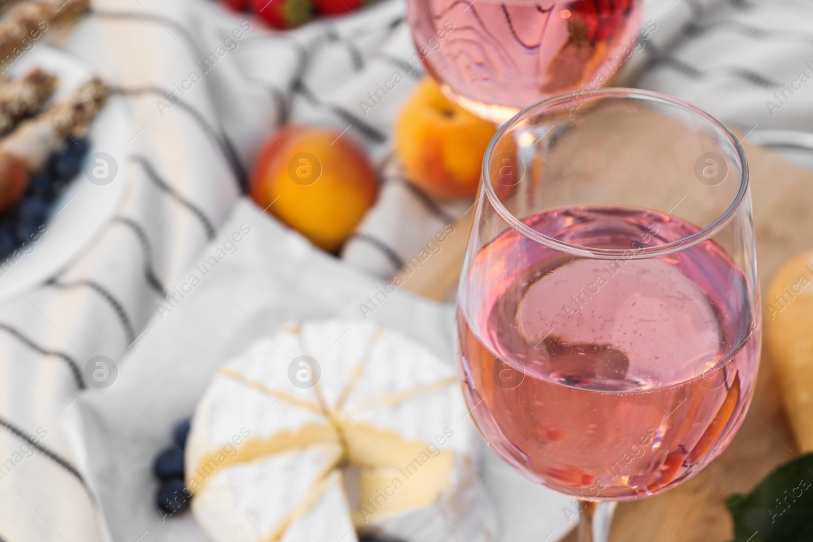 Photo of Glass of delicious rose wine and food on white picnic blanket, closeup