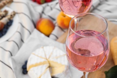 Glass of delicious rose wine and food on white picnic blanket, closeup