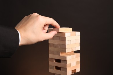 Photo of Playing Jenga. Man building tower with wooden blocks on dark background, closeup