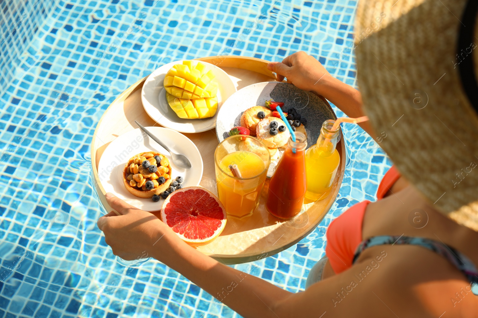 Photo of Young woman with delicious breakfast on floating tray in swimming pool, closeup