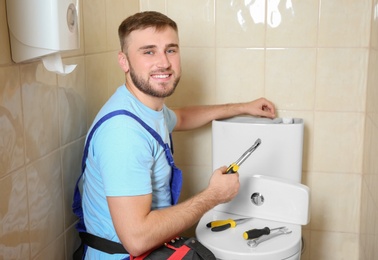 Photo of Professional plumber in uniform repairing toilet tank indoors