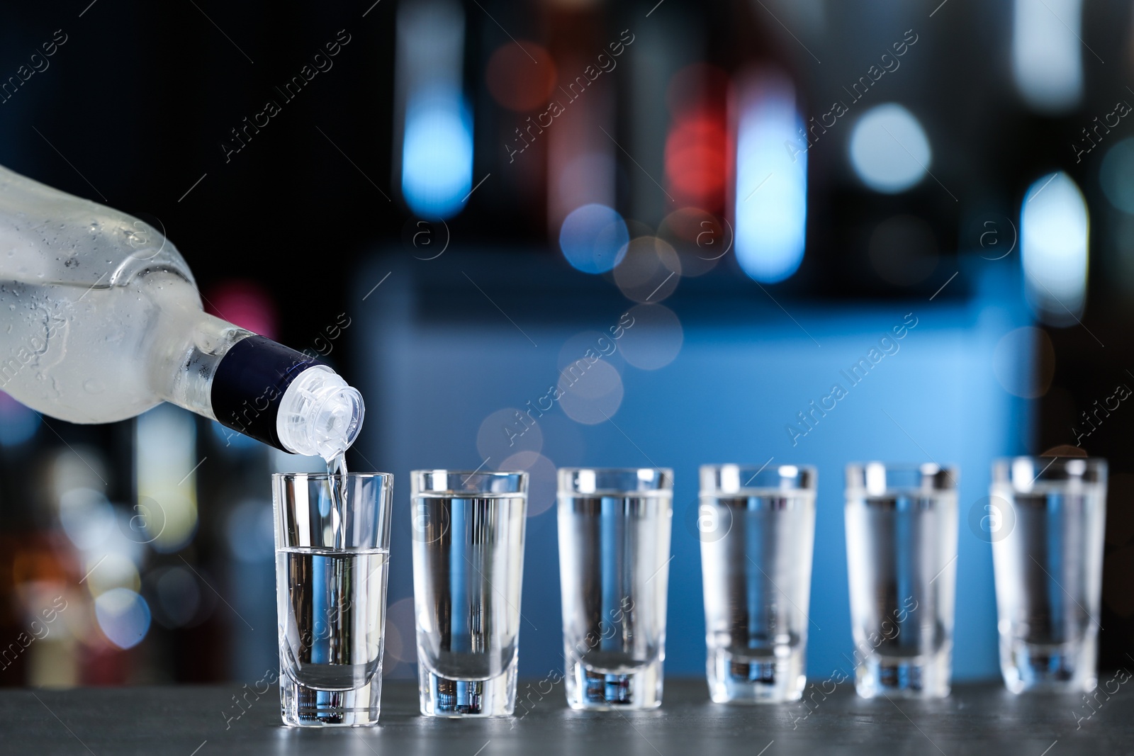 Photo of Pouring vodka from bottle into shot glasses on bar counter