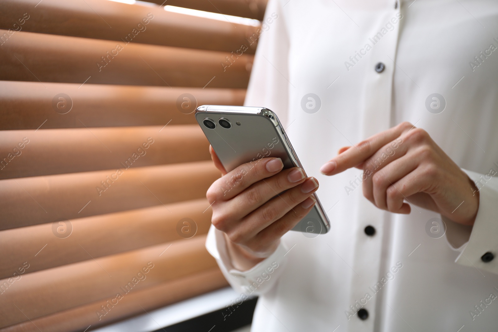 Photo of Young woman using modern smartphone near window indoors, closeup