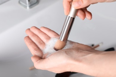 Photo of Woman washing makeup brush with soap, closeup