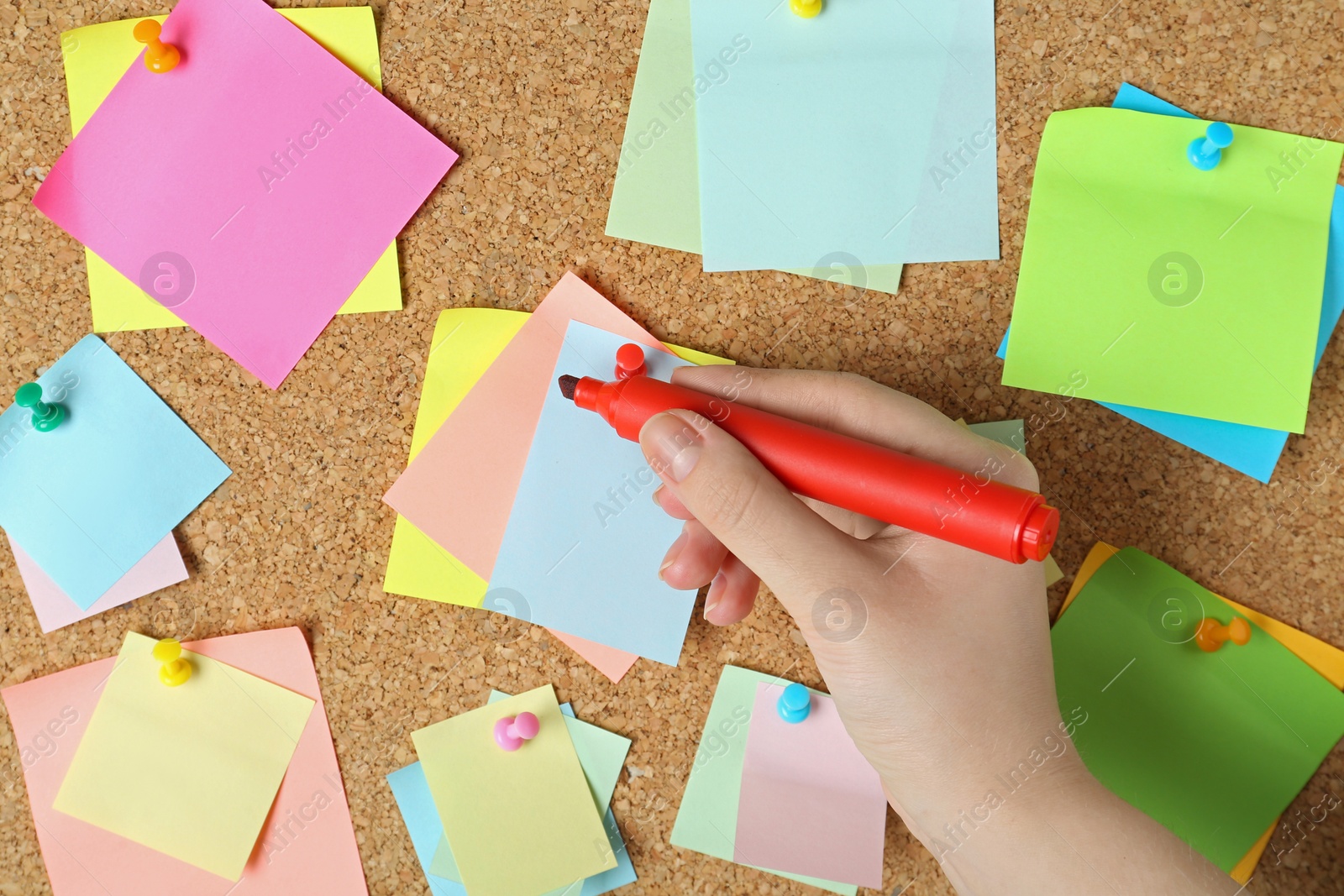 Photo of Woman writing on sticky note pinned to corkboard, closeup