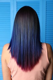 Photo of Young woman with bright dyed hair on blue wooden background, back view