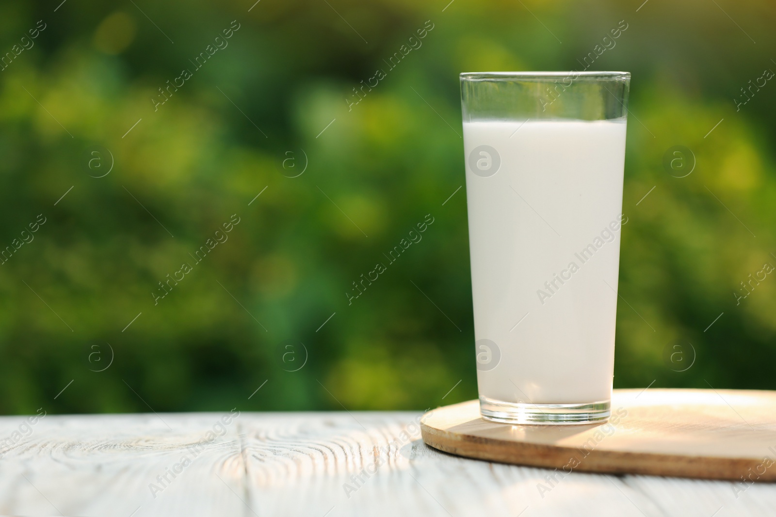 Photo of Glass of tasty fresh milk on white wooden table against blurred background, space for text
