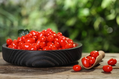 Photo of Plate and scoop with fresh goji berries on wooden table against blurred background. Space for text