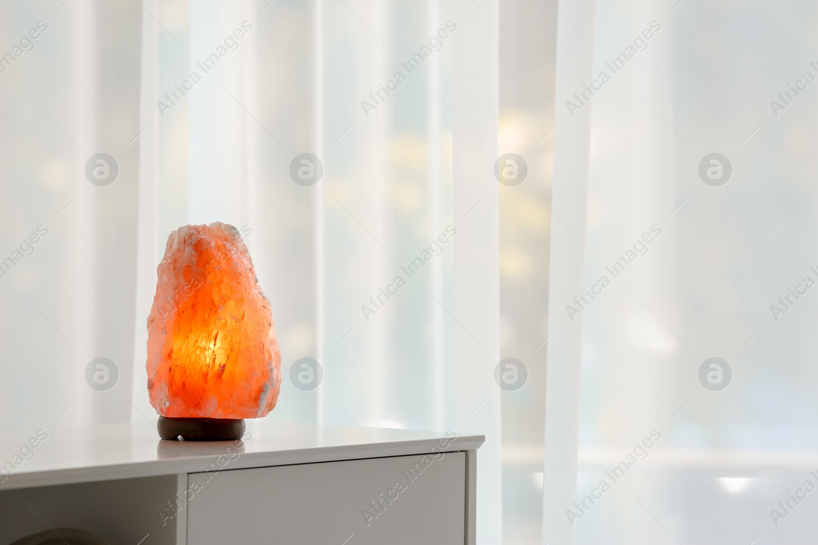 Photo of Himalayan salt lamp on cabinet against light background