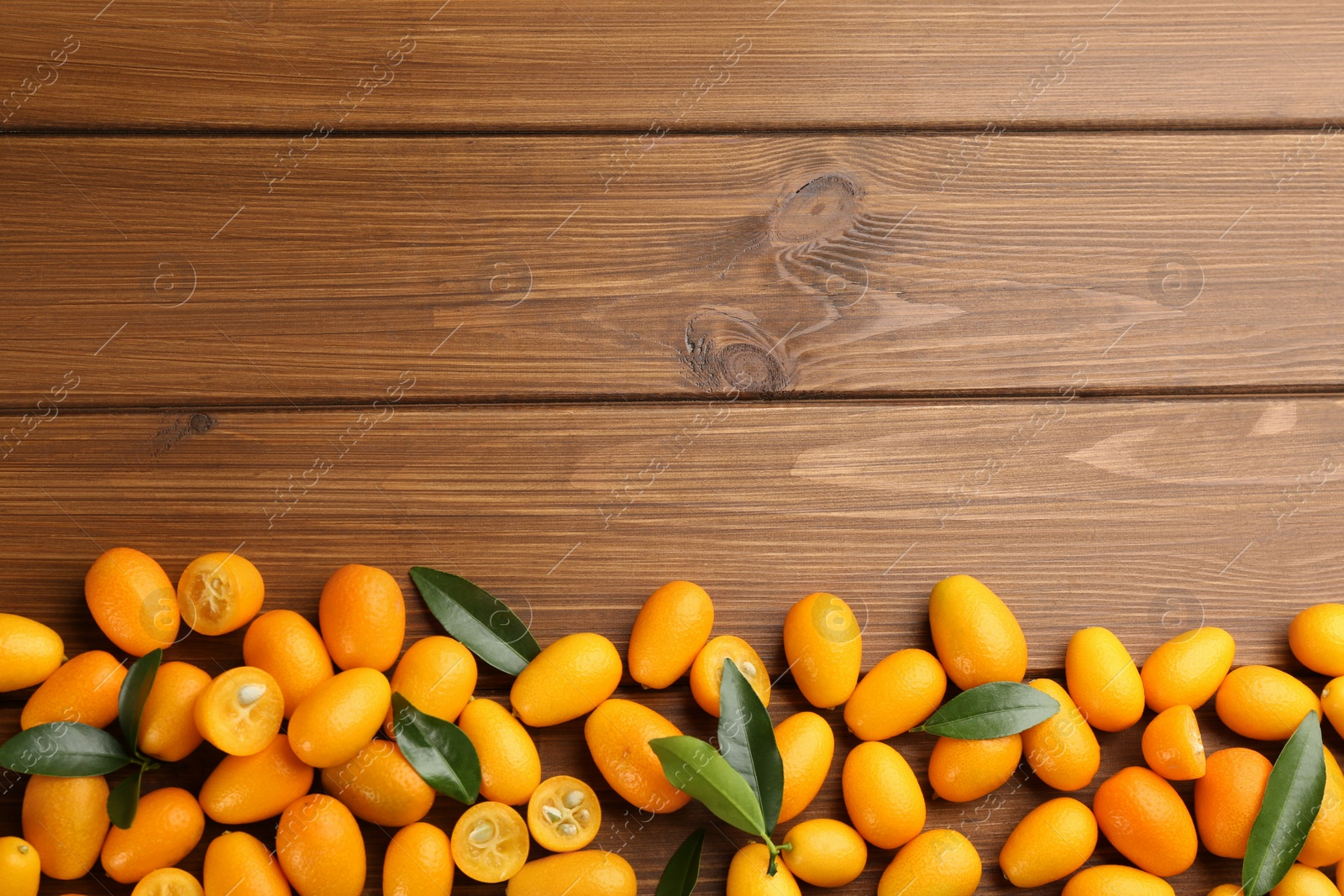 Photo of Fresh ripe kumquats with green leaves on wooden background, flat lay. Space for text