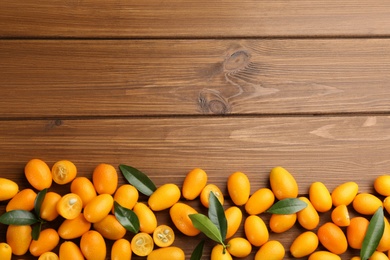 Fresh ripe kumquats with green leaves on wooden background, flat lay. Space for text