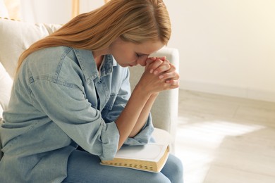 Photo of Religious young woman with Bible praying indoors. Space for text