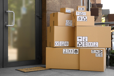 Photo of Cardboard boxes with different packaging symbols on porch near entrance. Parcel delivery