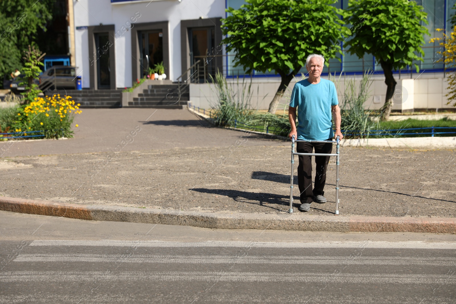 Photo of Elderly man crossing street with walking frame. Space for text