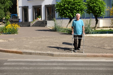 Photo of Elderly man crossing street with walking frame. Space for text