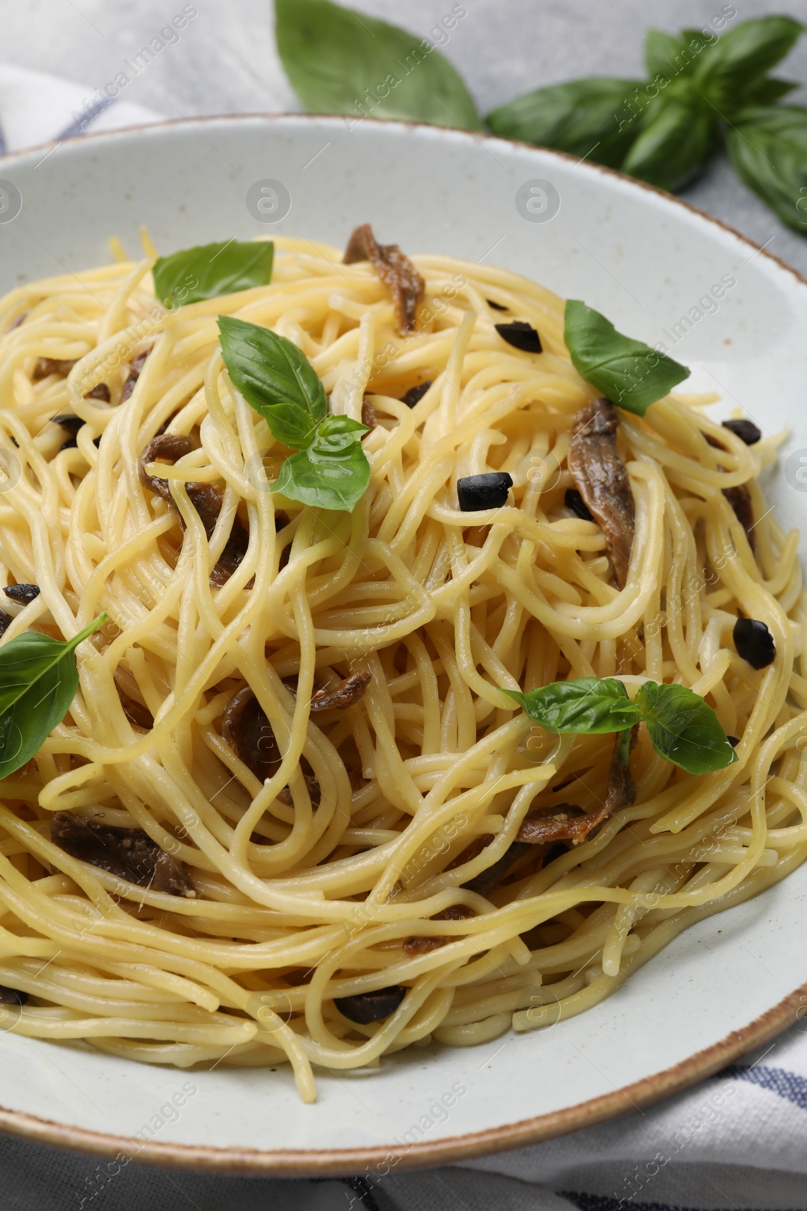 Photo of Delicious pasta with anchovies, olives and basil on plate, closeup