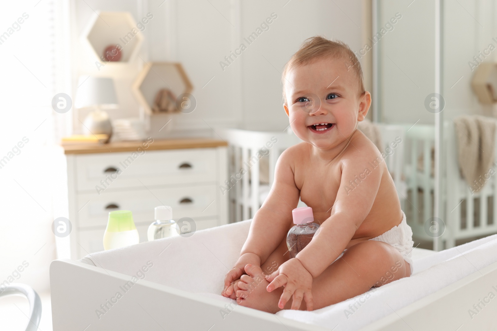 Photo of Cute little baby with bottle of massage oil on changing table at home