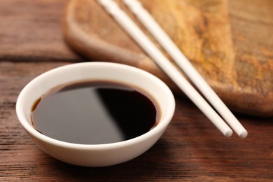 Photo of Bowl with soy sauce and chopsticks on wooden table, closeup