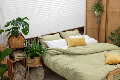 Photo of Comfortable bed and beautiful green houseplants in bedroom