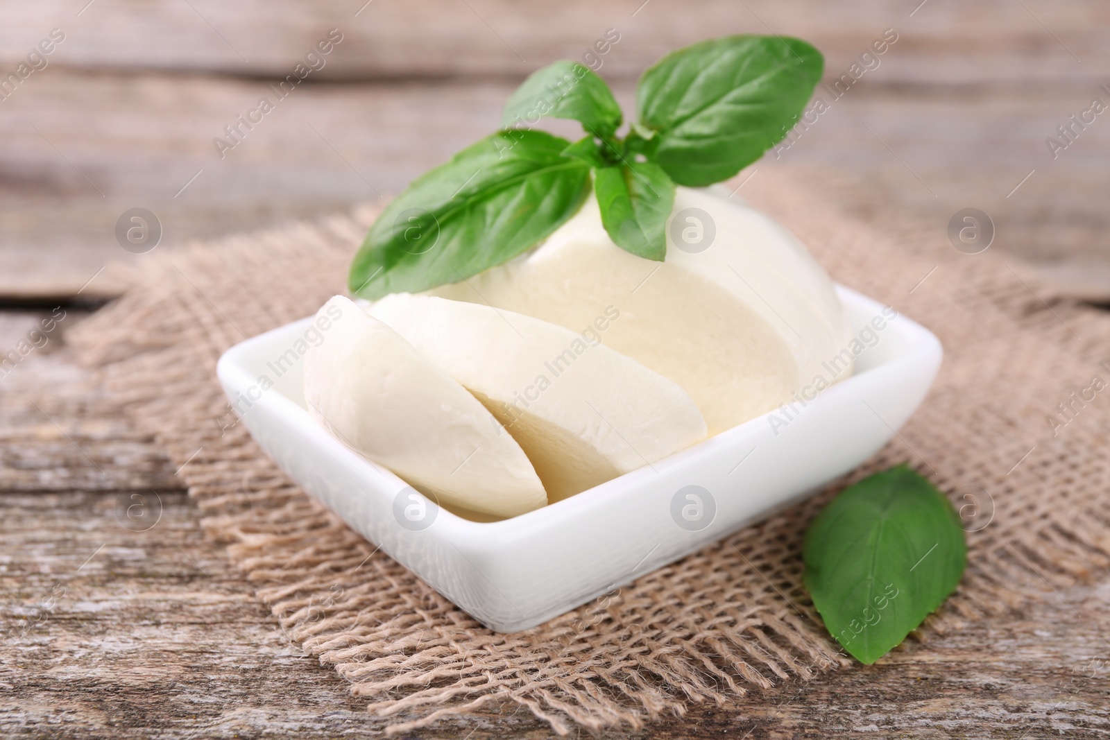 Photo of Cut mozzarella and basil leaves on wooden table, closeup