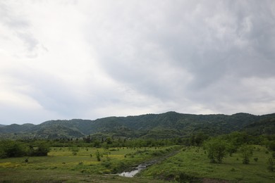 Photo of Picturesque view of mountains, trees and field on cloudy day