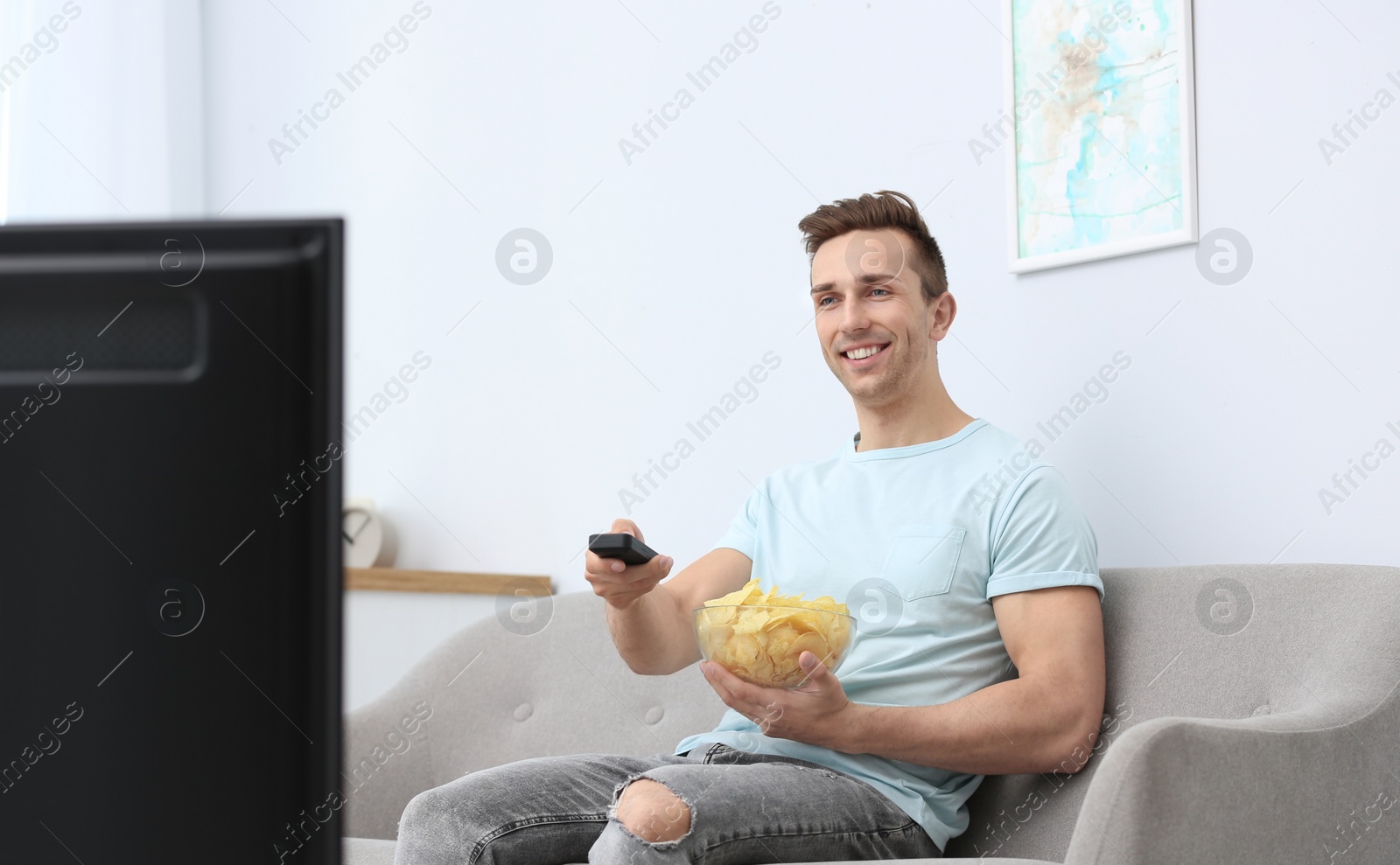 Photo of Man watching TV with bowl of potato chips in living room