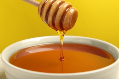 Photo of Pouring tasty honey from dipper into bowl against yellow background, closeup