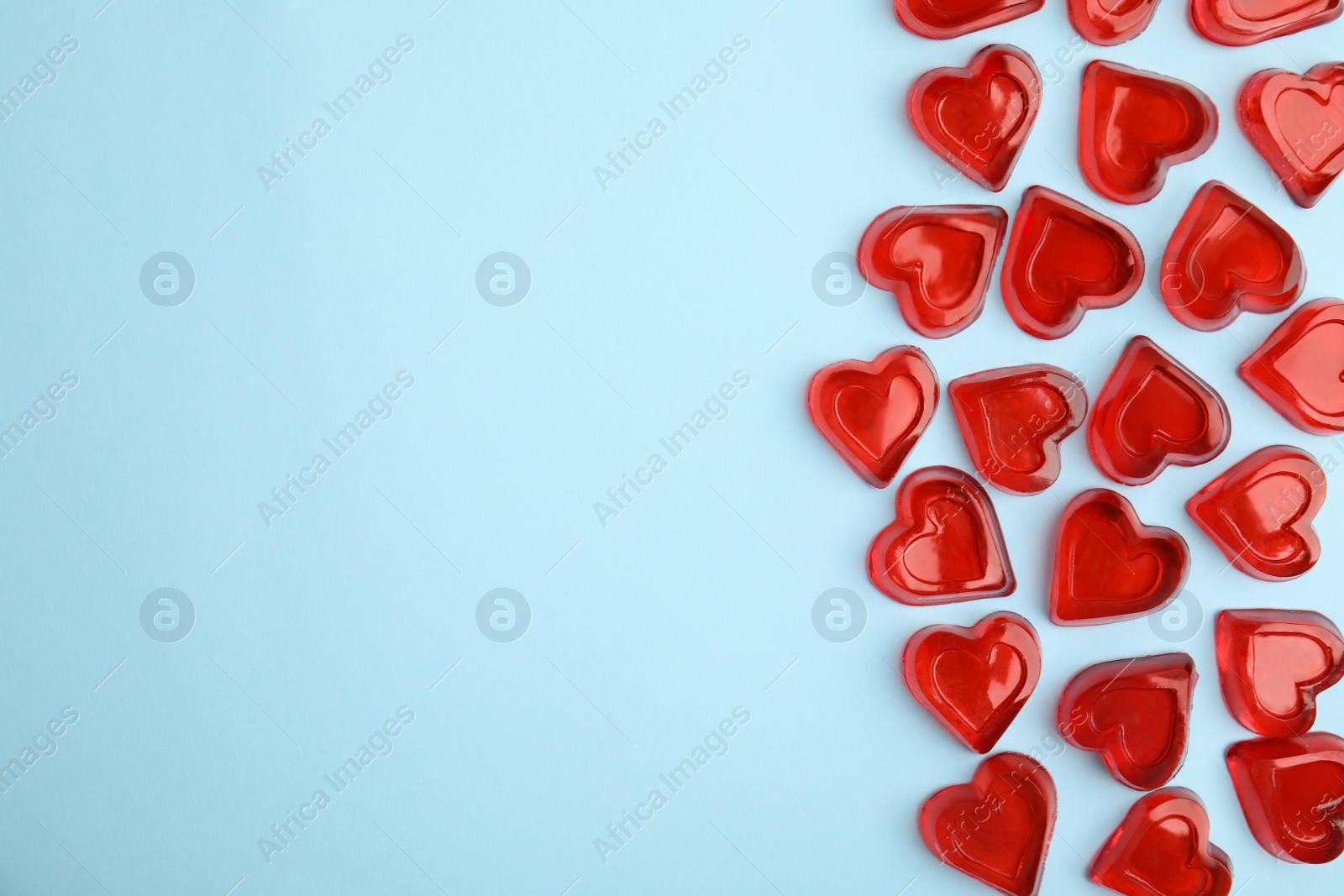 Photo of Sweet heart shaped jelly candies on light blue background, flat lay. Space for text