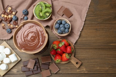 Photo of Fondue pot with melted chocolate, marshmallows, fresh kiwi and different berries on wooden table, flat lay. Space for text