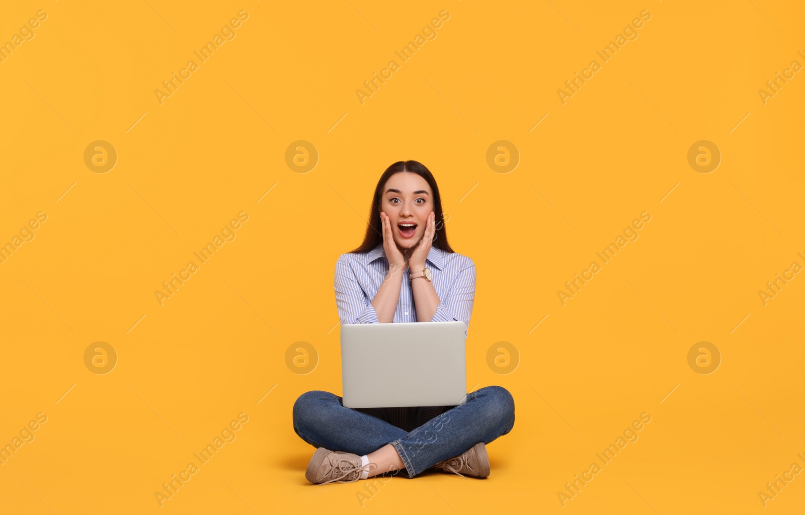 Photo of Surprised young woman with laptop on yellow background