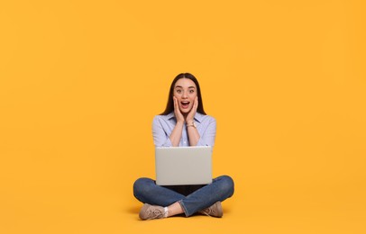 Photo of Surprised young woman with laptop on yellow background