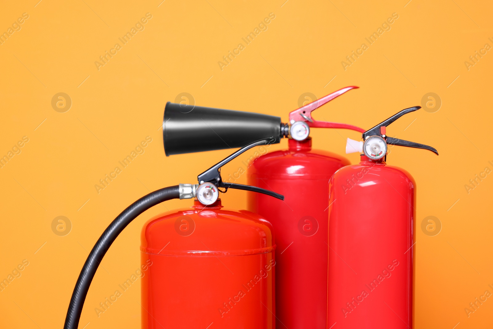 Photo of Three red fire extinguishers on orange background, closeup