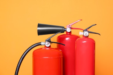 Photo of Three red fire extinguishers on orange background, closeup