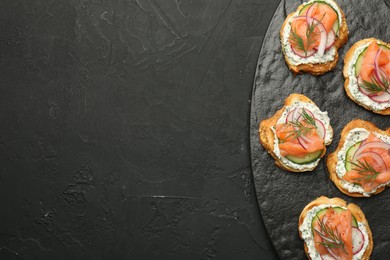 Photo of Tasty canapes with salmon, cucumber, radish and cream cheese on black table, top view. Space for text