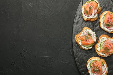 Tasty canapes with salmon, cucumber, radish and cream cheese on black table, top view. Space for text