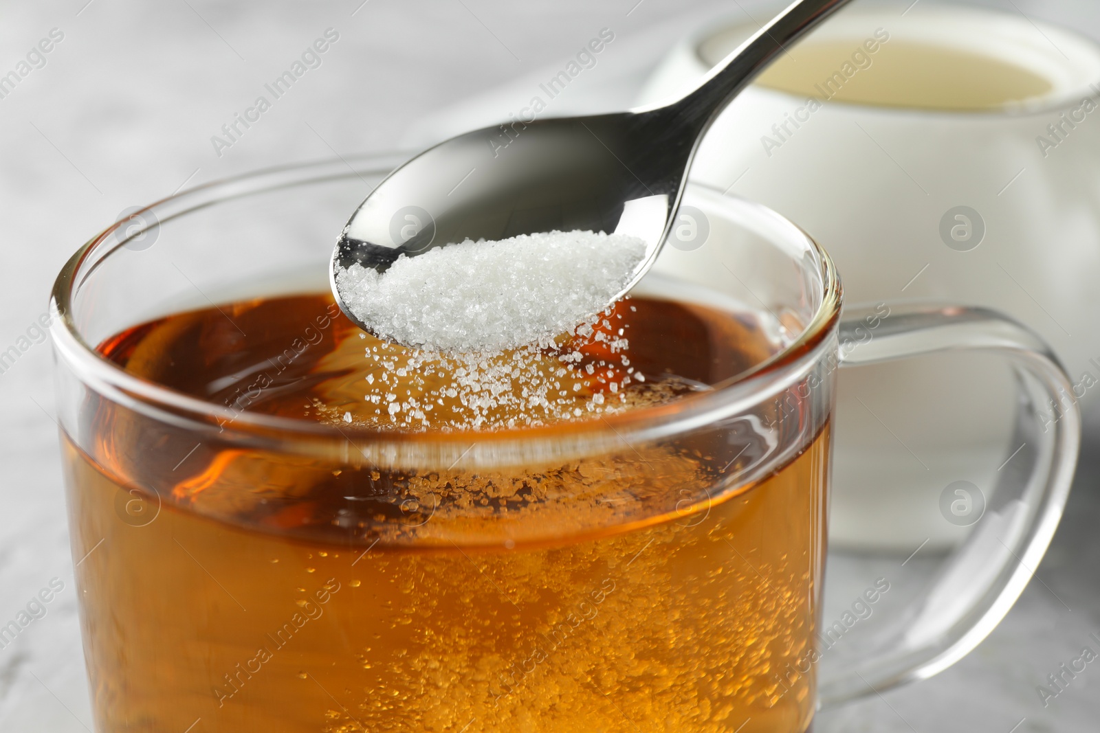 Photo of Adding sugar into cup of tea at table, closeup