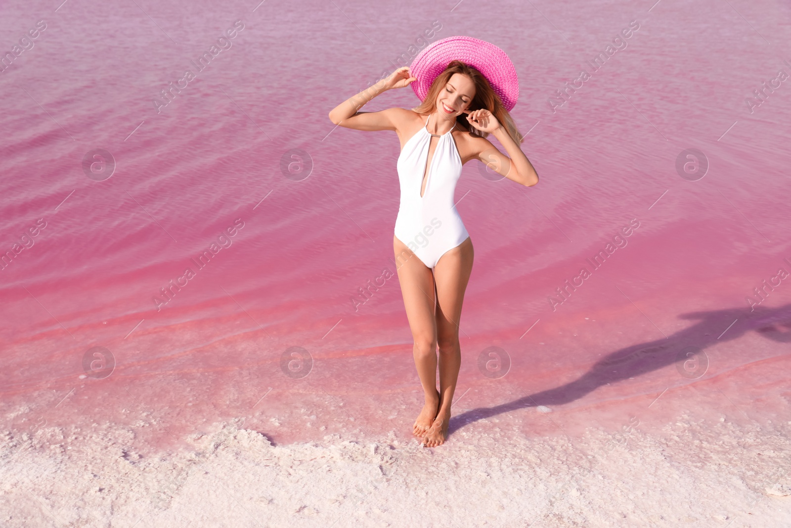 Photo of Beautiful woman in swimsuit posing near pink lake on sunny day