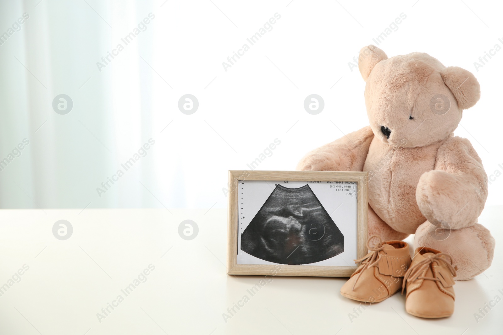 Photo of Ultrasound picture, teddy bear and baby shoes on table against light background. Space for text