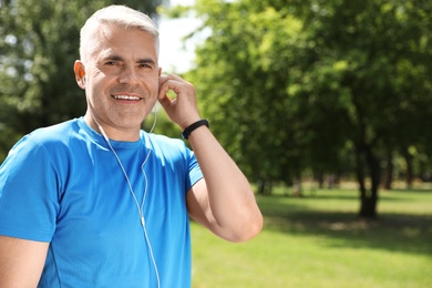 Photo of Handsome mature man listening to music in park, space for text. Healthy lifestyle