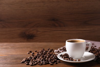 Cup of hot aromatic coffee and roasted beans on wooden table. Space for text