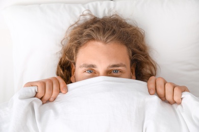 Photo of Young man covering his face with blanket while lying on pillow, top view. Bedtime