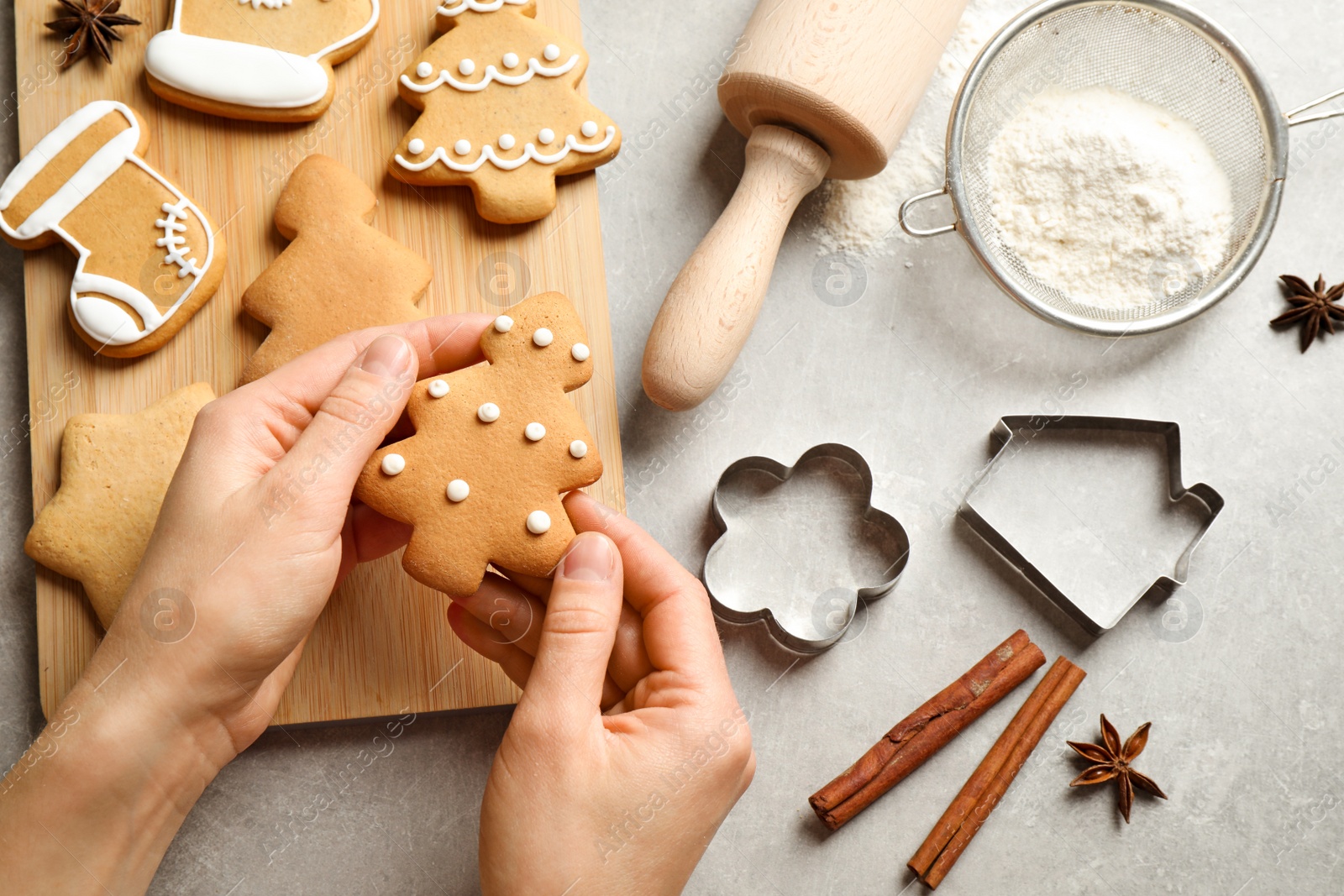 Photo of Woman holding tasty homemade Christmas cookie over grey table, top view