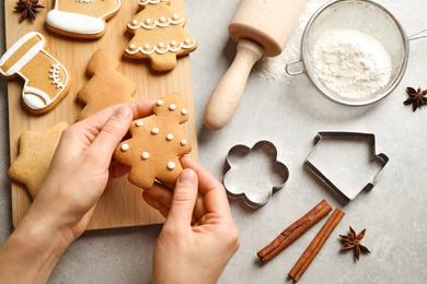 Photo of Woman holding tasty homemade Christmas cookie over grey table, top view